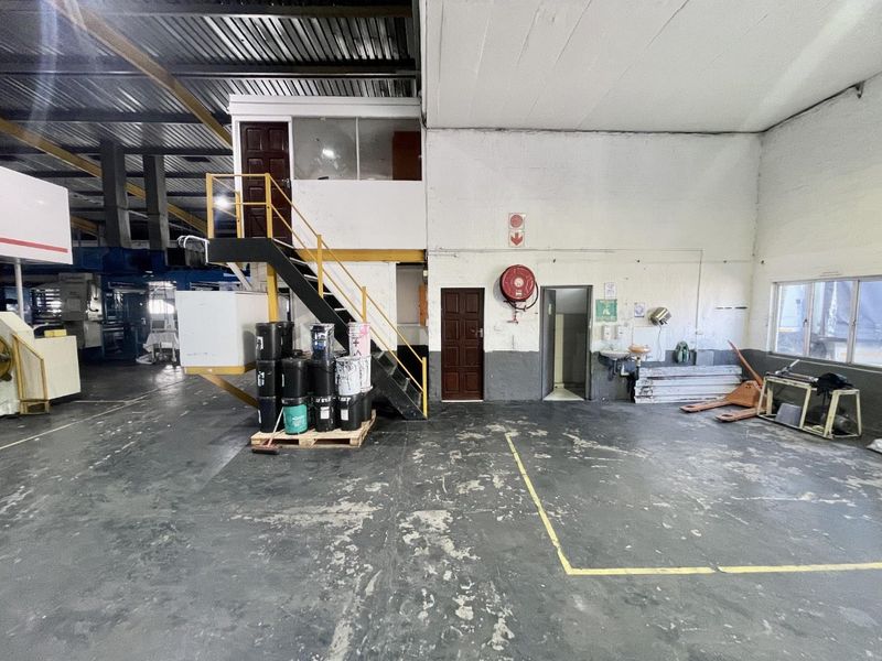 Industrial warehouse space featuring a mezzanine level, steel staircase, and functional wash area with exposed structural elements and durable flooring.