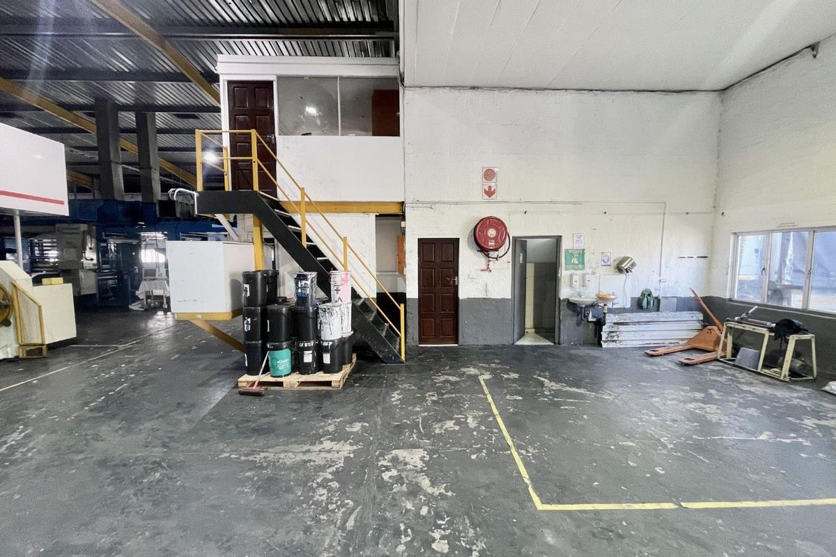Industrial warehouse space featuring a mezzanine level, steel staircase, and functional wash area with exposed structural elements and durable flooring.