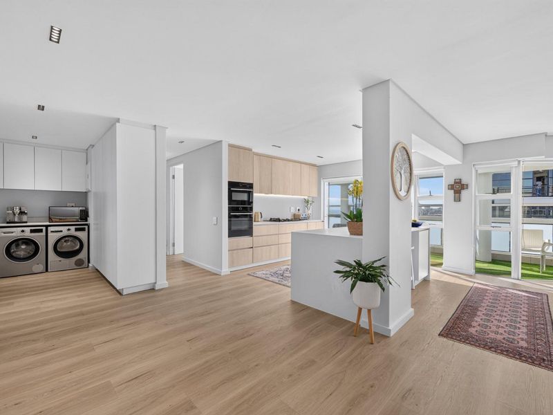 Modern open-plan living area featuring a sleek kitchen with integrated appliances, light wood cabinetry, and seamless access to a private balcony.