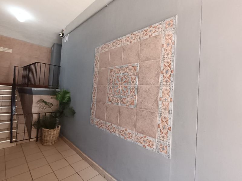 A communal hallway area featuring tiled flooring, a decorative tiled wall feature, and a staircase with a metal railing.