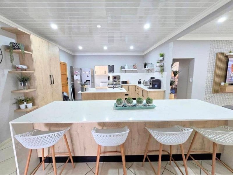 Modern open-plan kitchen featuring a large central island with quartz countertops, light wood cabinetry, and recessed lighting, creating a bright and functional living space.