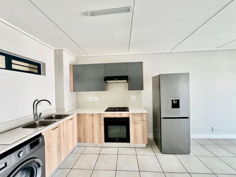 Modern kitchen featuring light wood-finish lower cabinetry, grey upper cabinets, tiled backsplash, built-in oven, electric hob, and a double sink with a mixer tap.