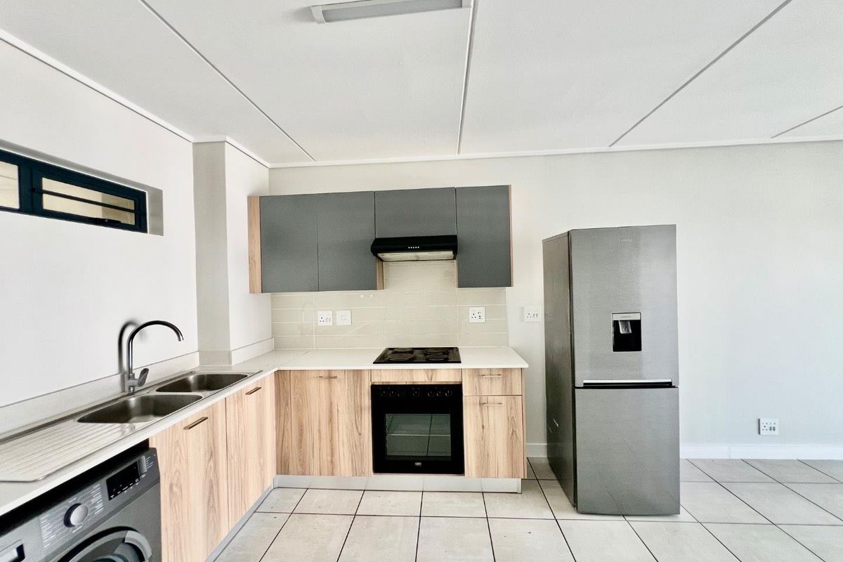 Modern kitchen featuring light wood-finish lower cabinetry, grey upper cabinets, tiled backsplash, built-in oven, electric hob, and a double sink with a mixer tap.