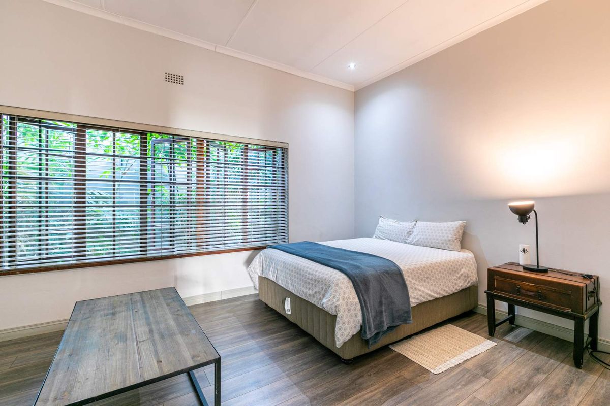 A well-maintained bedroom featuring modern laminate flooring, neutral wall tones, and large windows fitted with venetian blinds for natural light control.