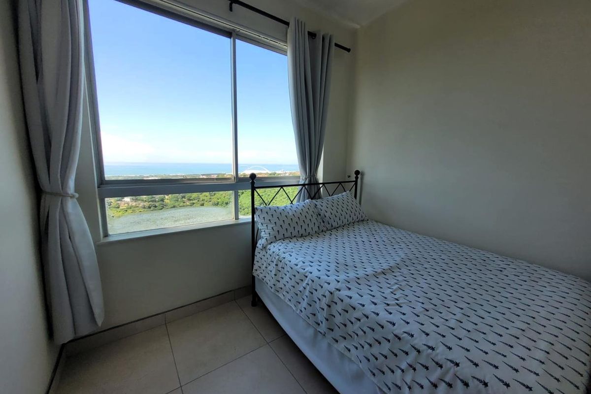 A bright bedroom featuring large windows with scenic coastal views and tiled flooring.