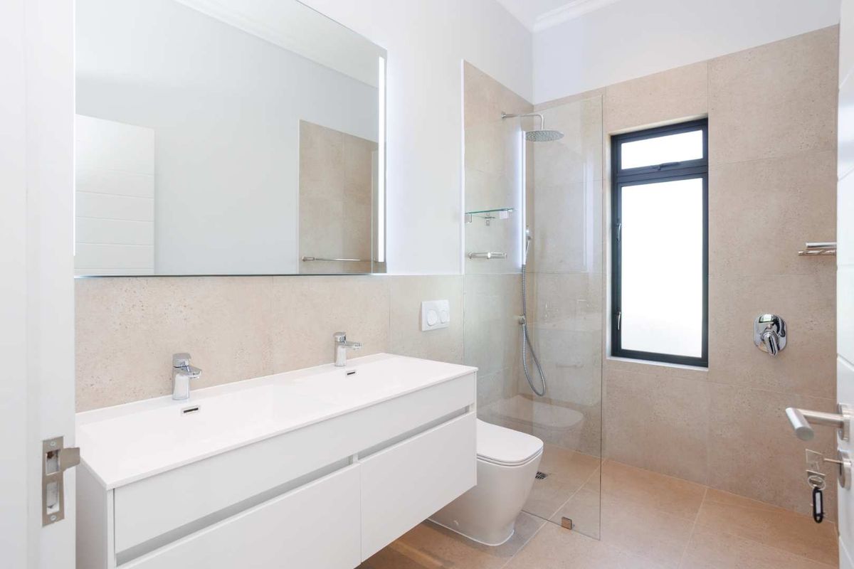 Modern bathroom featuring a double vanity with integrated sinks, a frameless glass shower enclosure, and neutral wall and floor tiling.