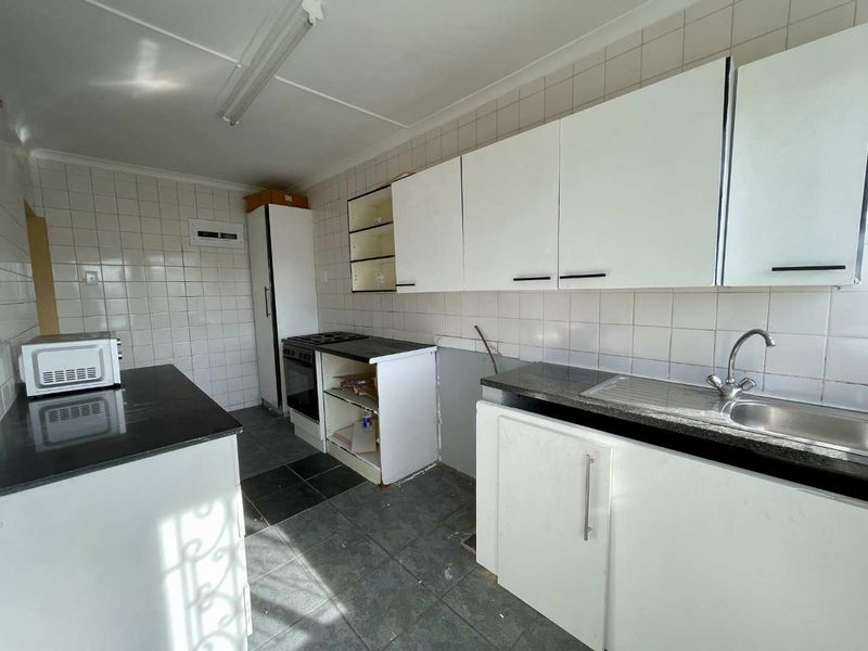 A functional kitchen space featuring built-in cabinetry, a stainless steel sink, and a built-in oven, currently requiring cosmetic updates and repairs.