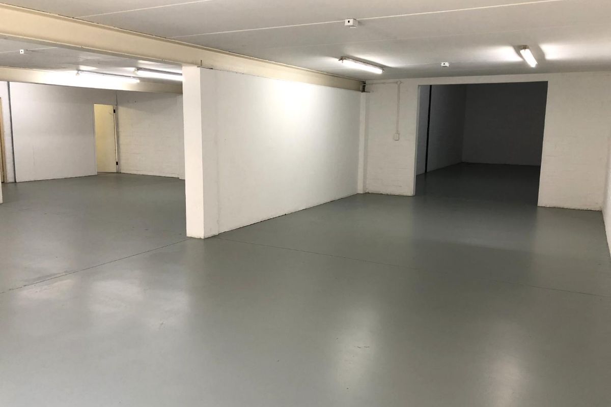 A spacious, open-plan utility or storage area featuring durable epoxy flooring, clean white walls, and functional overhead fluorescent lighting.