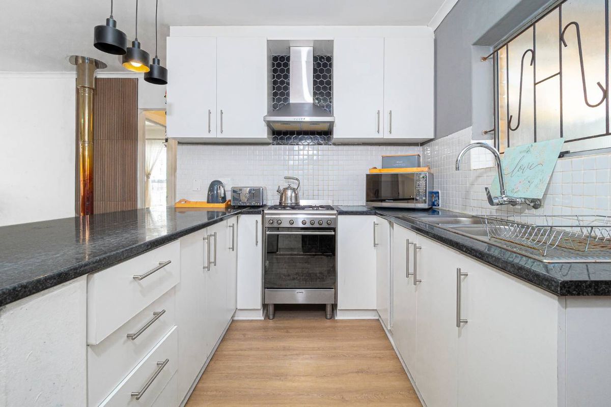 A well-maintained kitchen featuring white cabinetry, dark granite countertops, a stainless steel oven with extractor fan, and a tiled backsplash.