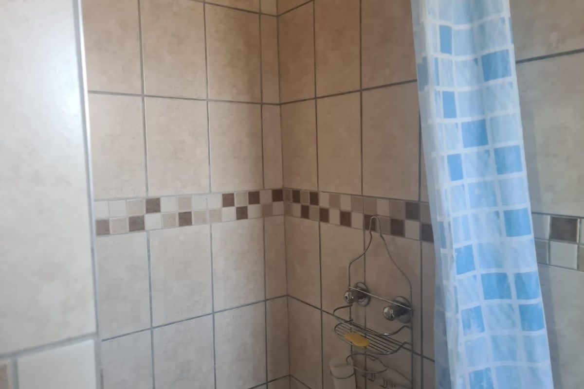 A functional shower area featuring neutral ceramic wall tiles with a decorative mosaic border.
