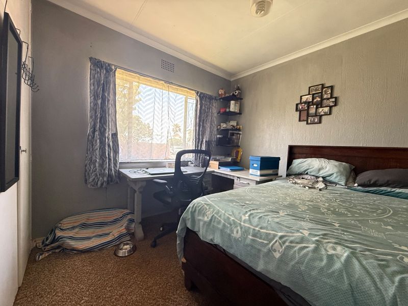A bedroom featuring carpet flooring, coved ceilings, and a window, currently used as a combined sleeping and workspace area.