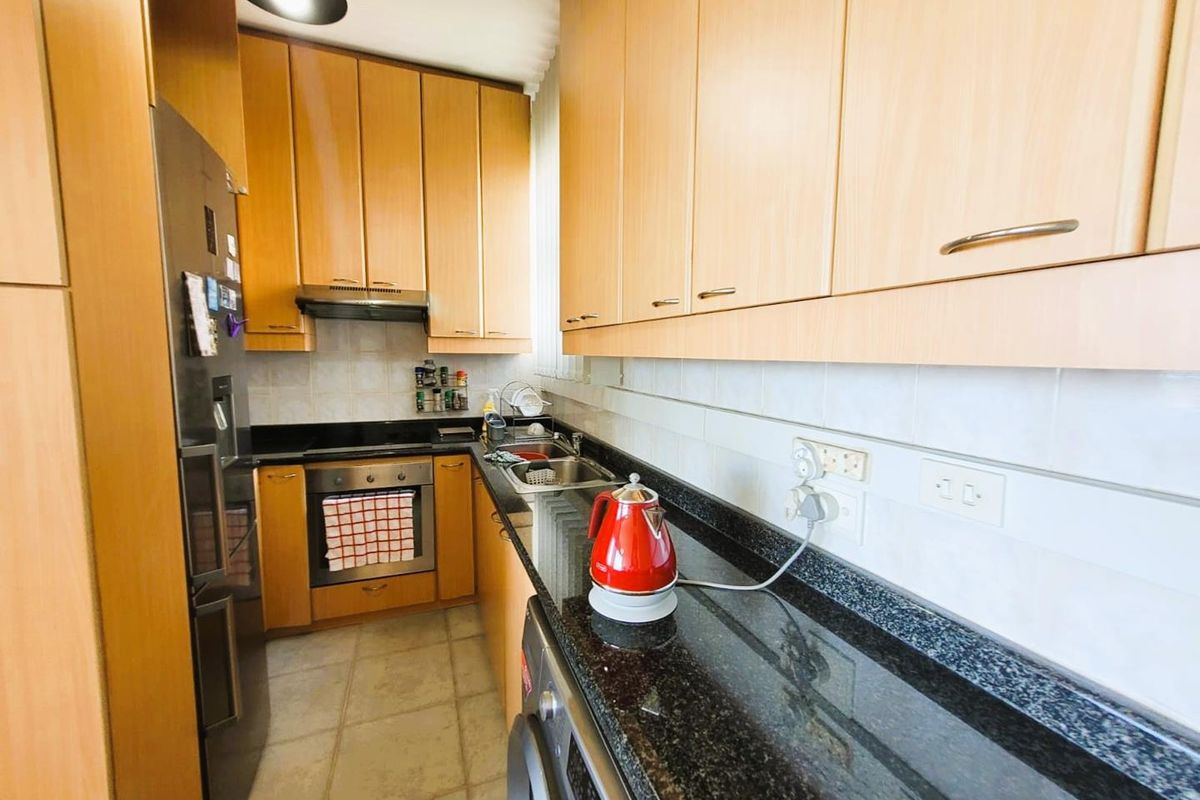 A compact galley-style kitchen featuring light wood-toned cabinetry, dark granite countertops, a built-in oven, and an integrated extractor fan.