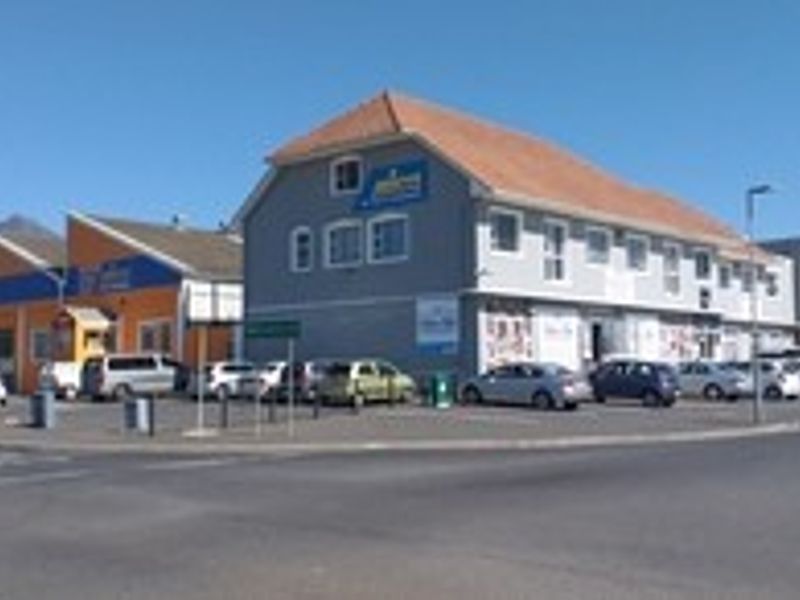 A street-level view of a multi-unit commercial office complex featuring a paved parking area and multi-level building facades.