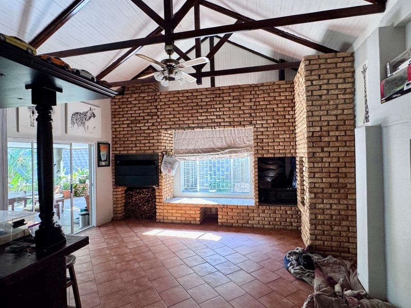 Spacious living room featuring a vaulted timber-beamed ceiling, exposed brick fireplace, and large sliding glass doors leading to an outdoor patio area.
