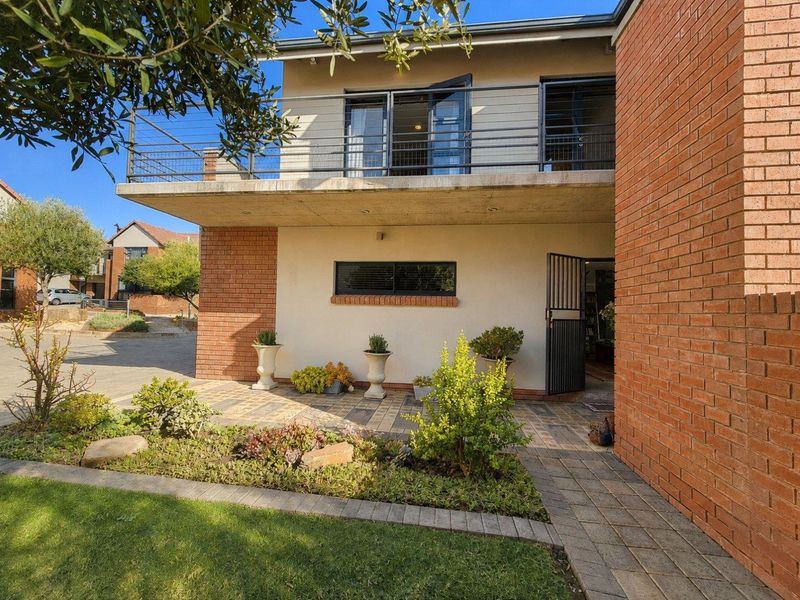 Rear view of the townhouse featuring a paved patio area, a landscaped garden, and an upper-level balcony with metal railings.