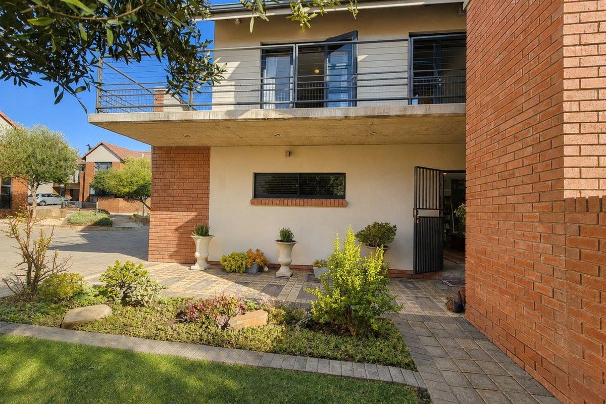 Rear view of the townhouse featuring a paved patio area, a landscaped garden, and an upper-level balcony with metal railings.