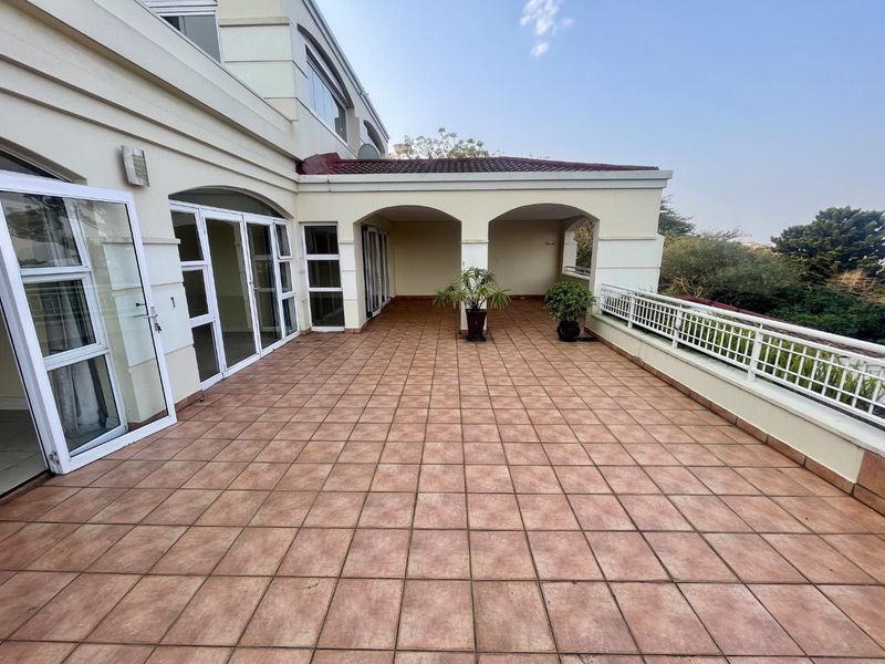 Spacious covered balcony featuring tiled flooring, arched architectural details, and a metal balustrade, offering an open outdoor living area.