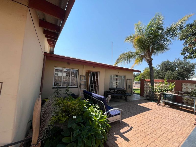 A rear exterior view featuring a paved patio area, security gates on windows and doors, and a decorative breeze block boundary wall.