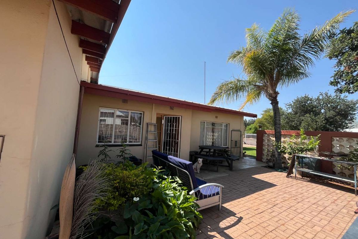 A rear exterior view featuring a paved patio area, security gates on windows and doors, and a decorative breeze block boundary wall.