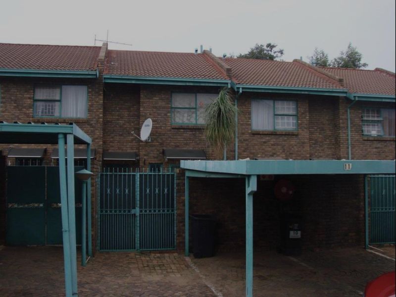 Front elevation of a brick apartment complex featuring covered carports, security gates, and tiled roofing.