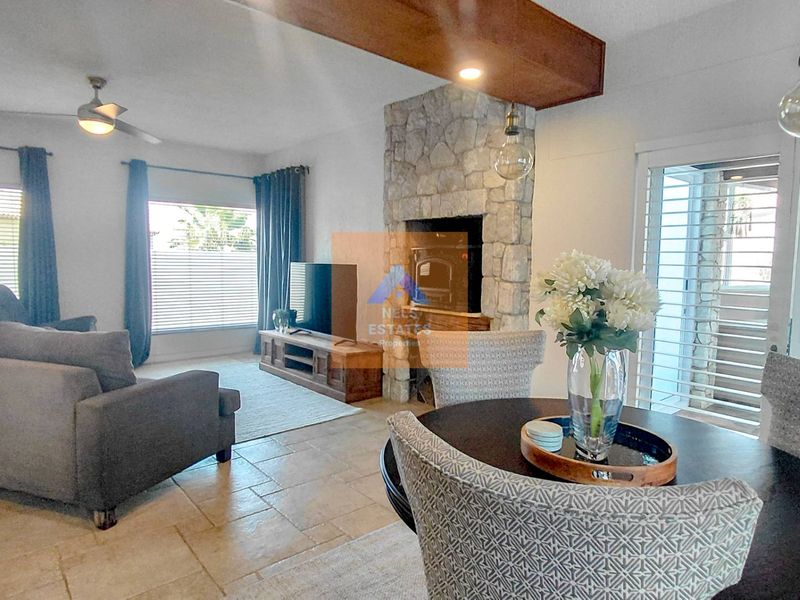 Spacious open-plan living and dining area featuring a prominent stone fireplace, tiled flooring, and an exposed timber ceiling beam.
