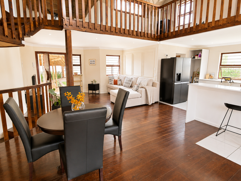 Spacious open-plan living and dining area featuring timber flooring, a mezzanine level with wooden balustrades, and a modern kitchen with a breakfast bar.