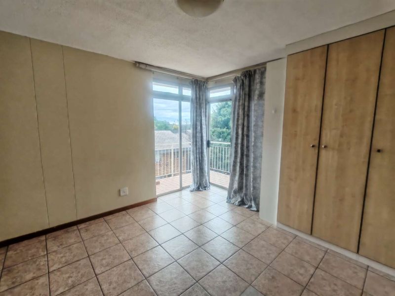 A bright, empty bedroom featuring tiled flooring, built-in cupboards, and sliding glass doors that open onto a private balcony.