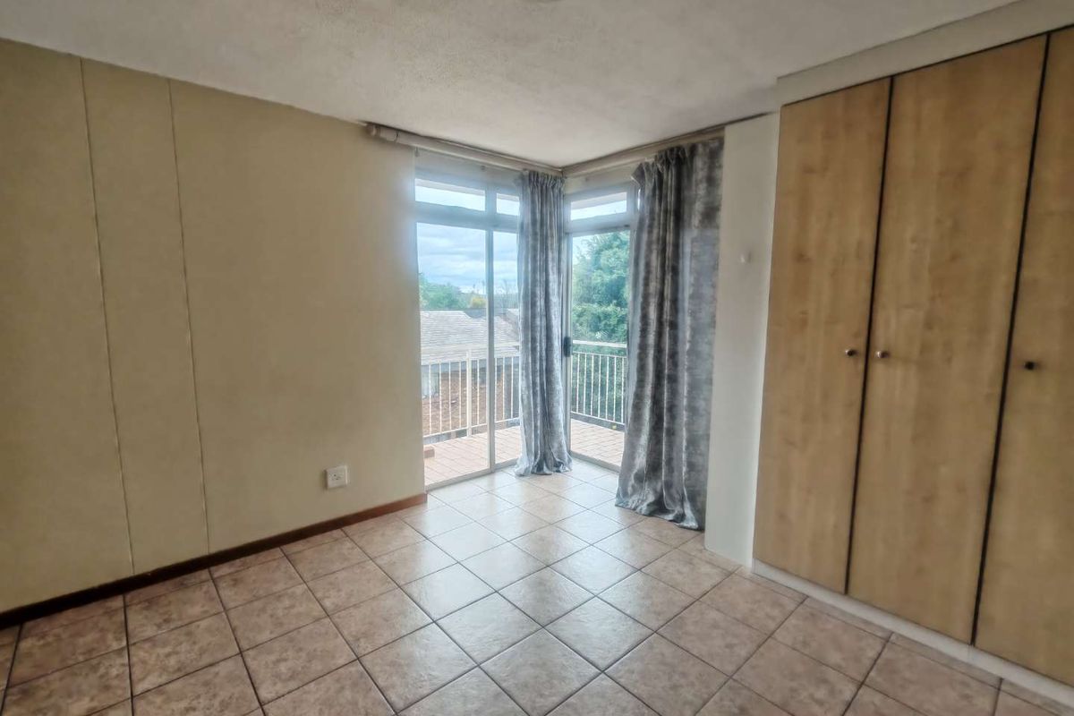 A bright, empty bedroom featuring tiled flooring, built-in cupboards, and sliding glass doors that open onto a private balcony.