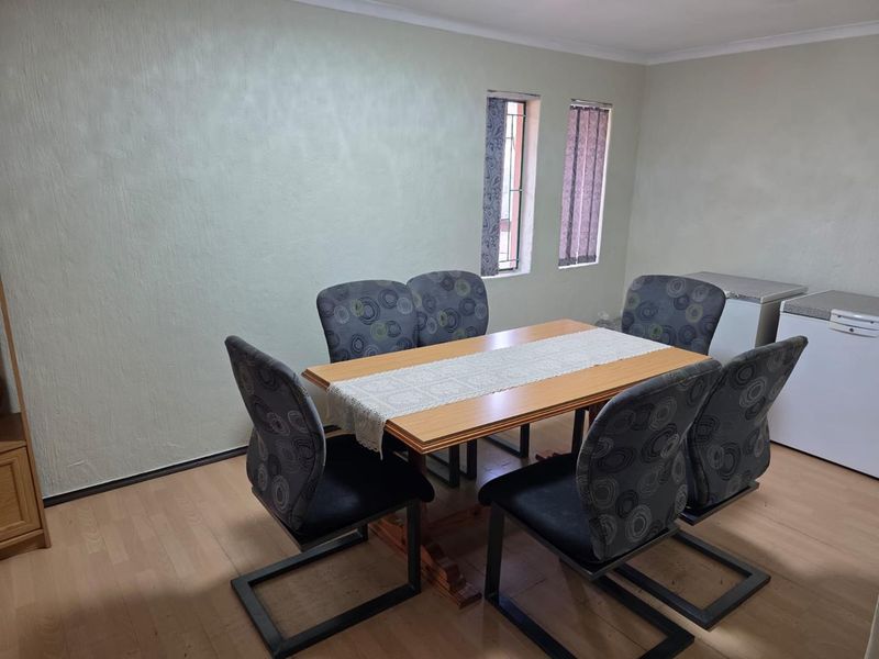 A functional dining area featuring laminate flooring, coved ceilings, and dual vertical windows providing natural light.