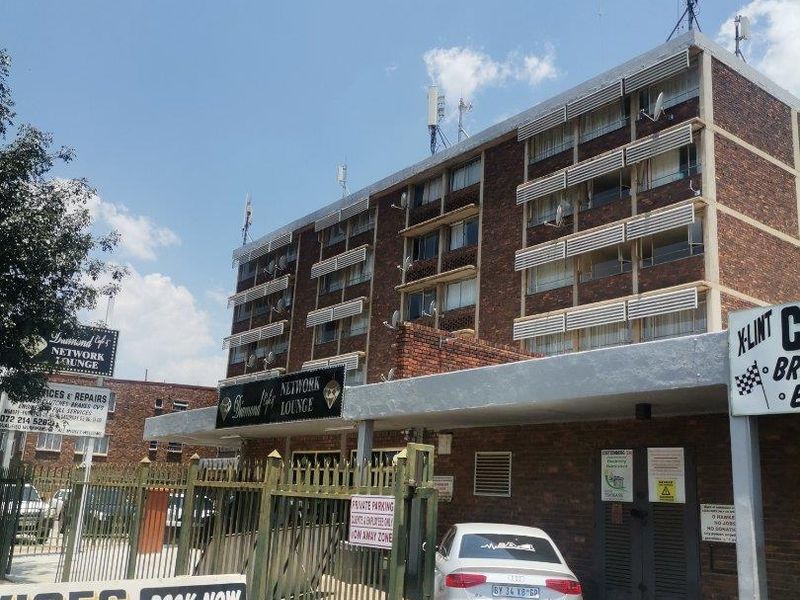 Exterior view of a multi-story brick apartment building featuring a gated entrance, security fencing, and various commercial signage on the premises.