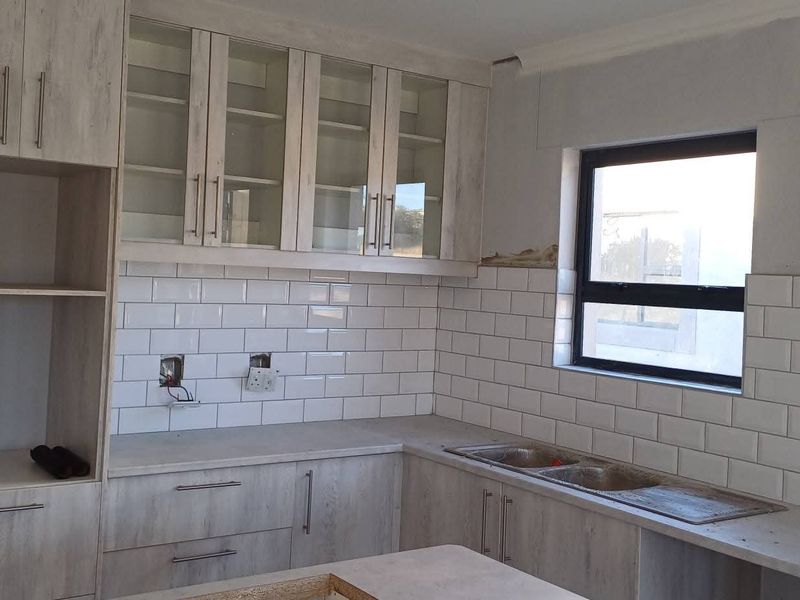 An unfinished kitchen space featuring light wood-look cabinetry, white subway tile backsplash, and a double bowl sink, currently awaiting final installation and electrical finishing.