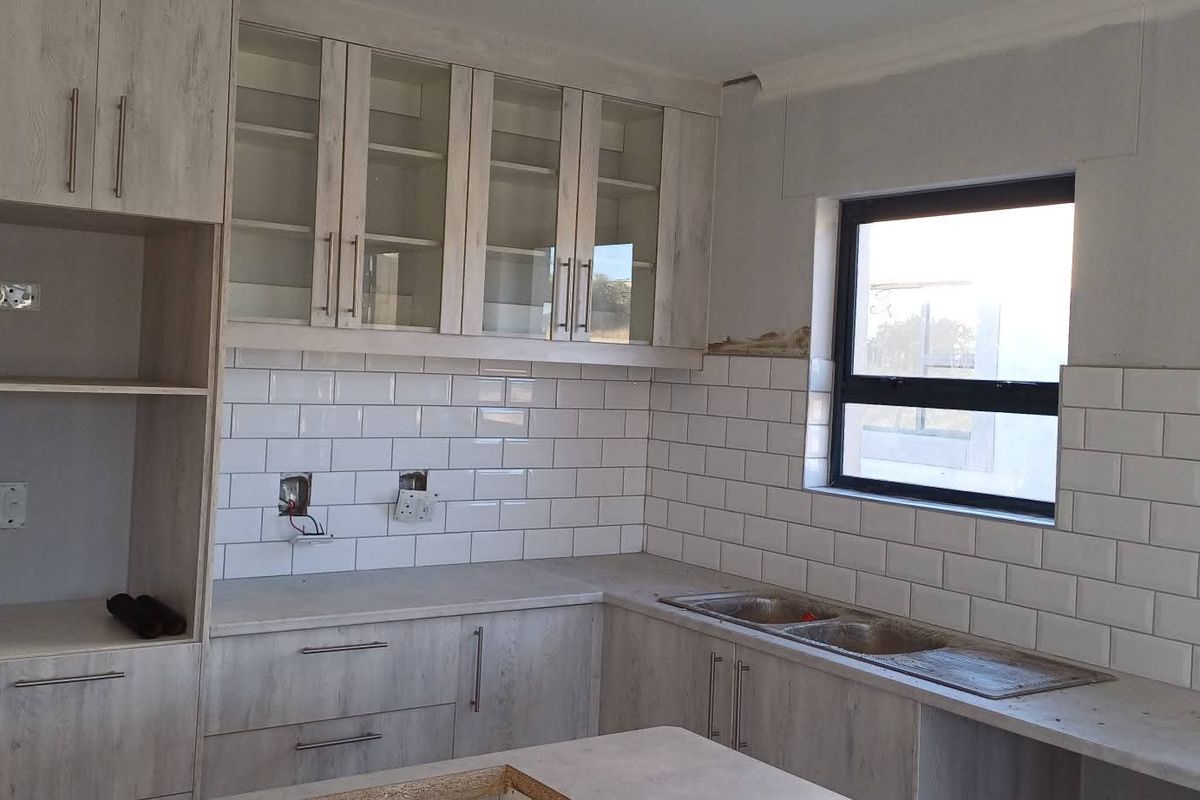 An unfinished kitchen space featuring light wood-look cabinetry, white subway tile backsplash, and a double bowl sink, currently awaiting final installation and electrical finishing.