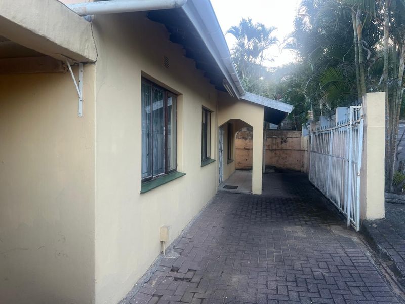 Side exterior view of the townhouse featuring a paved walkway, metal security gate, and perimeter retaining wall with visible signs of wear.