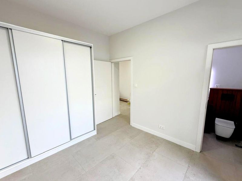 A bright bedroom featuring large format floor tiles, a built-in sliding door wardrobe, and direct access to an en-suite bathroom.