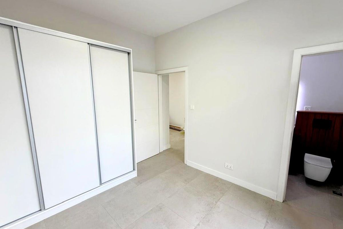 A bright bedroom featuring large format floor tiles, a built-in sliding door wardrobe, and direct access to an en-suite bathroom.