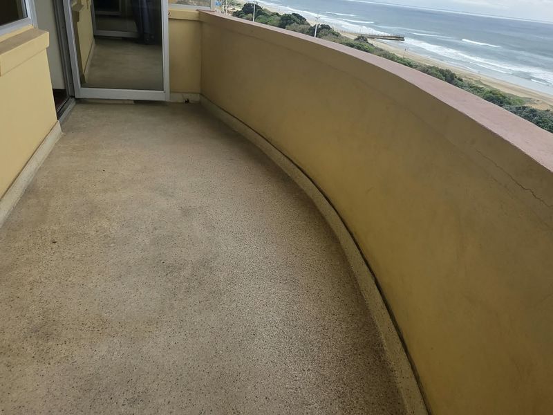 A curved balcony featuring a solid wall railing and direct ocean views, offering potential for outdoor seating and relaxation.