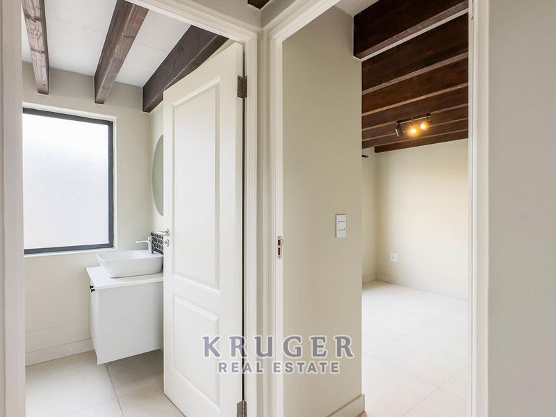 A bright hallway featuring exposed timber ceiling beams, tiled flooring, and a modern vanity area with a vessel sink.