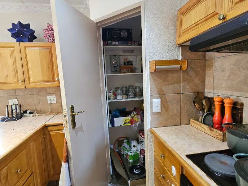 A functional kitchen featuring wooden cabinetry, built-in oven, extractor fan, and a convenient walk-in pantry cupboard with tiled flooring throughout.