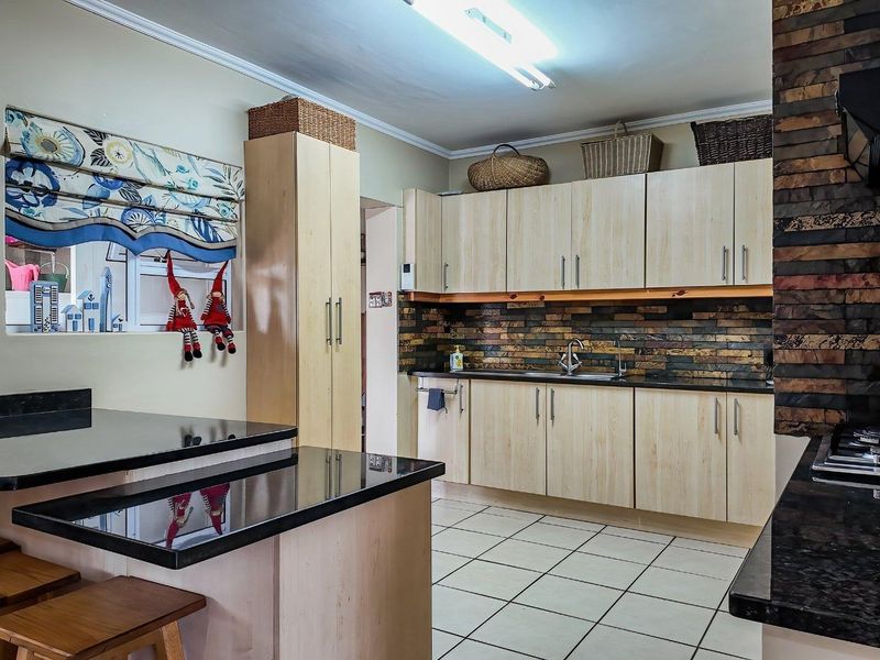 Functional kitchen featuring light wood-look cabinetry, dark granite countertops, a decorative stone tile backsplash, and ceramic floor tiling.