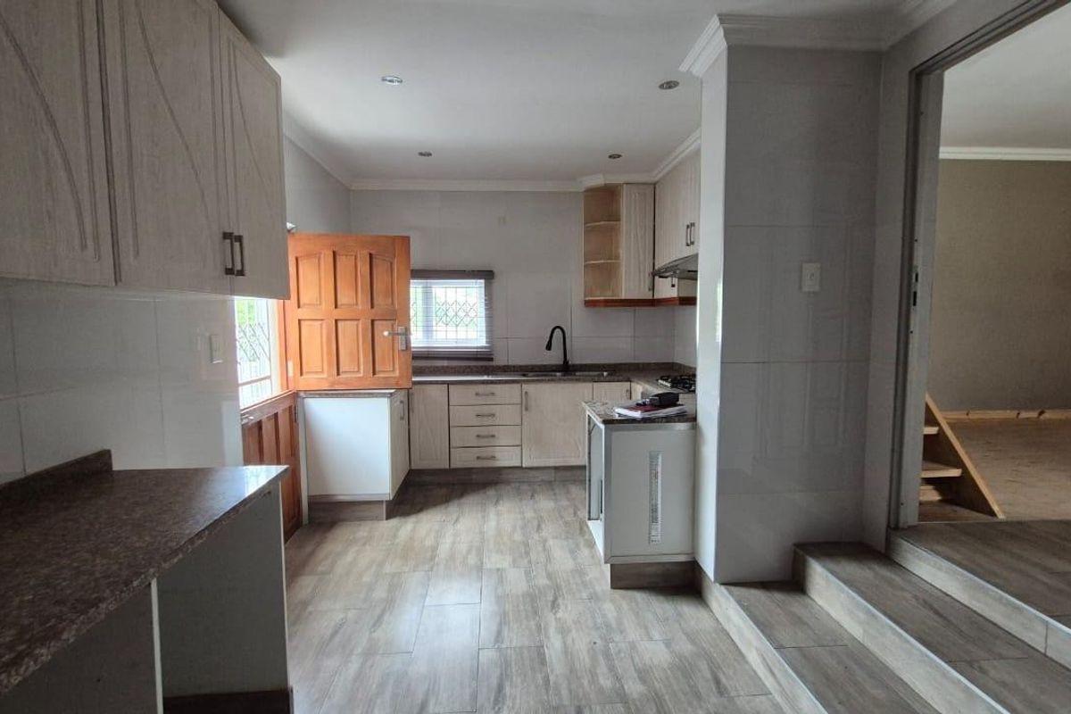 A functional kitchen featuring built-in cabinetry, laminate countertops, and tiled flooring, with an open-plan layout leading to an adjacent living area.