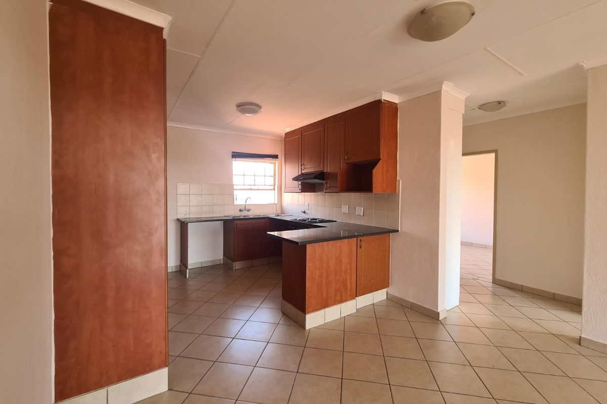 A functional kitchen featuring wooden cabinetry, dark countertops, a built-in hob, and tiled flooring, offering a practical layout for daily meal preparation.