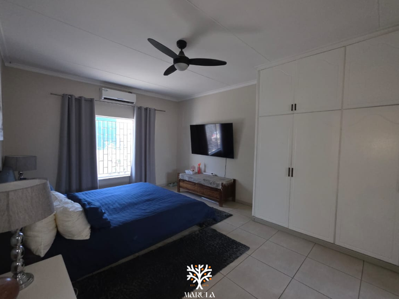 A well-maintained bedroom featuring built-in cupboards, tiled flooring, a ceiling fan, and a split-system air conditioner for climate control.