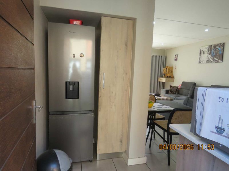 An open-plan living area featuring tiled flooring, recessed lighting, and a built-in pantry cupboard adjacent to the kitchen space.