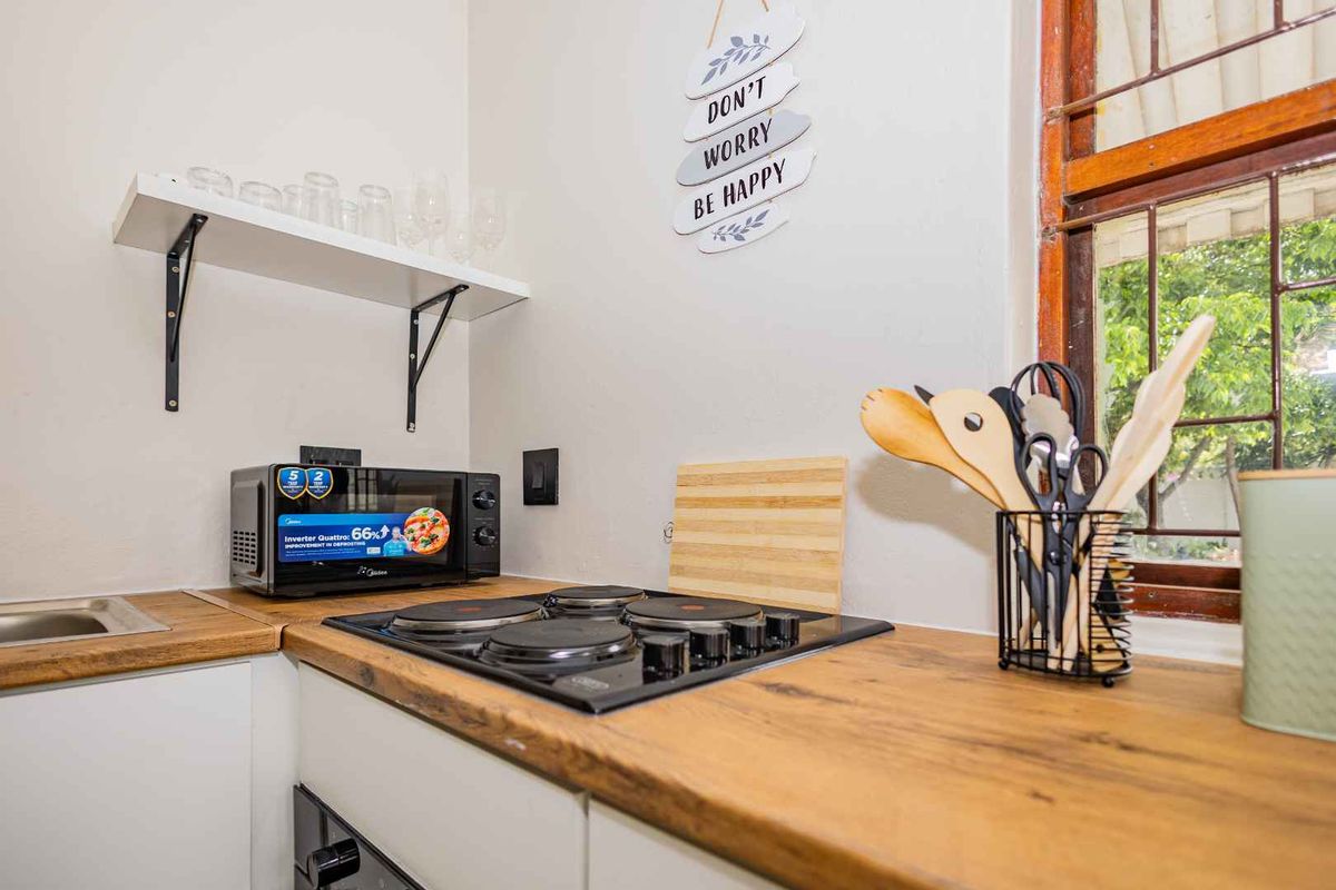 Compact kitchen area featuring a built-in electric hob, wooden countertops, and a wall-mounted shelf, providing a functional workspace.