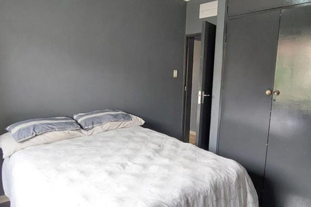 A bedroom featuring dark painted walls and a built-in wardrobe with overhead storage compartments.
