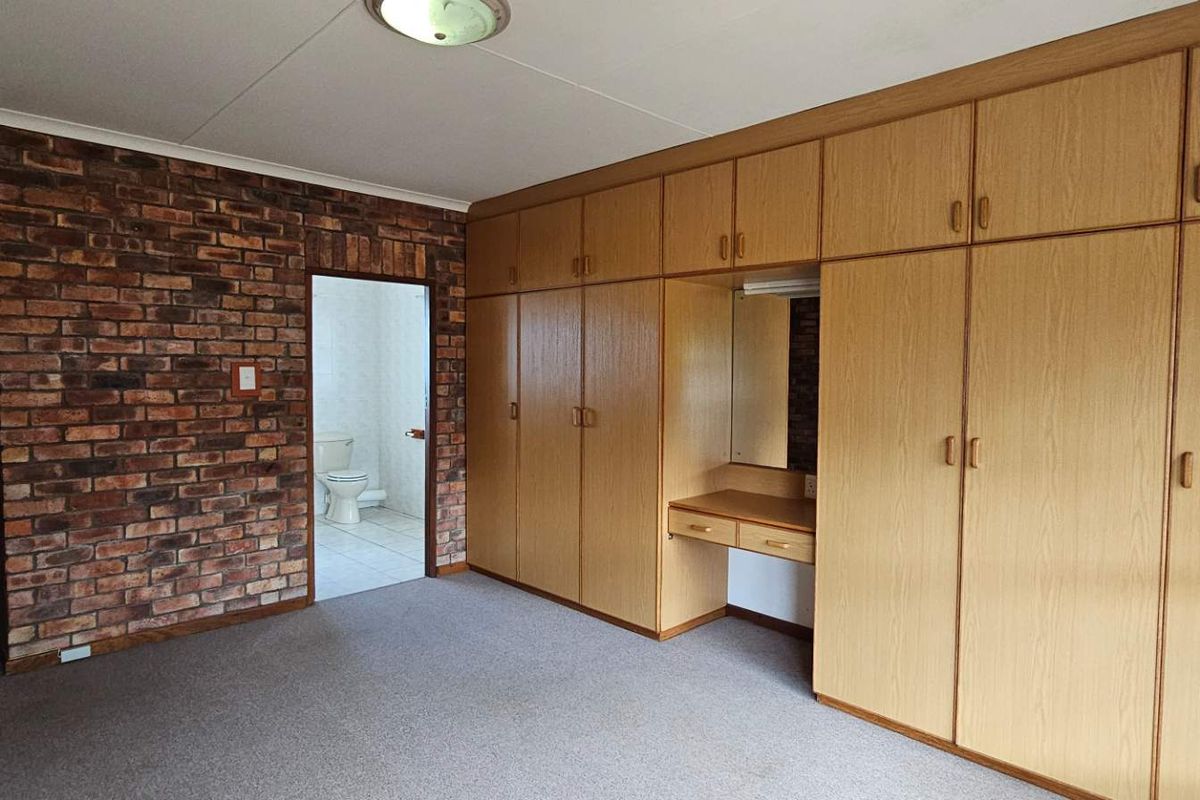 Spacious bedroom featuring extensive built-in wooden cabinetry with an integrated vanity, exposed brick feature wall, and direct access to an en-suite bathroom.