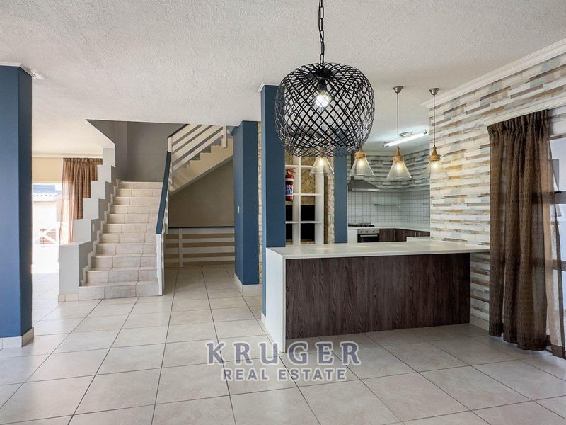Spacious open-plan living area featuring a modern kitchen island, tiled flooring, and a central staircase leading to the upper level.