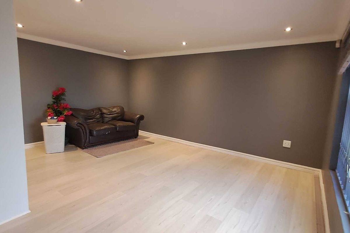 A spacious living room featuring light-toned laminate flooring, recessed ceiling lighting, and neutral grey walls, offering a clean and versatile living space.