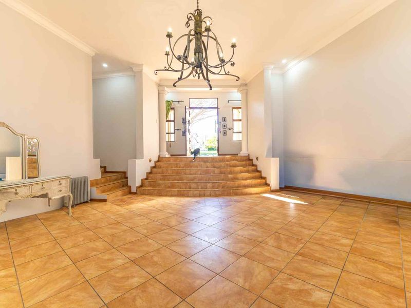Spacious entrance hall featuring tiled flooring, a grand wrought iron chandelier, and a raised platform leading to the main front door.