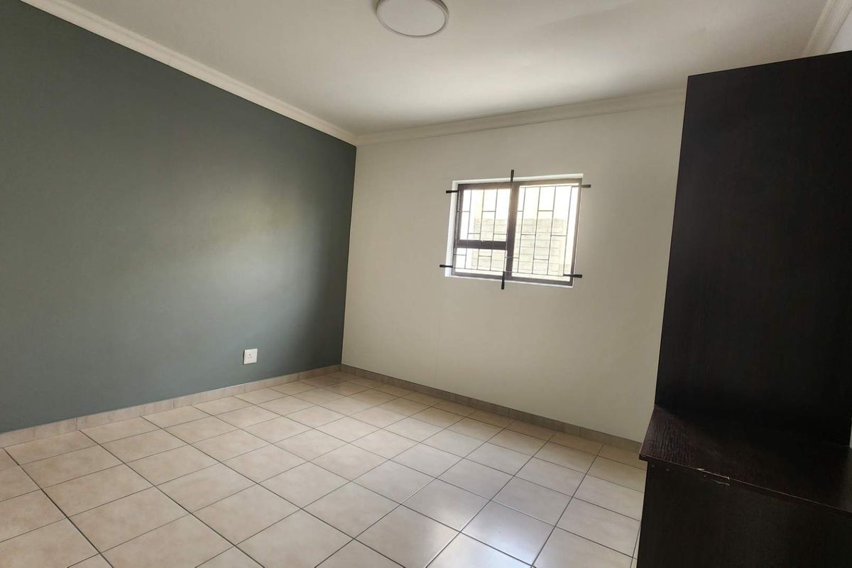 A clean, empty bedroom featuring neutral tiled flooring, a dark accent wall, and a window fitted with security bars.